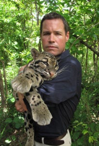 Jeff Corwin holding a wild cat with a green, leafy jungle background