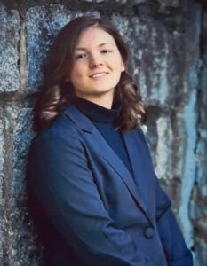 A woman in a blue blazer leans against a stone wall